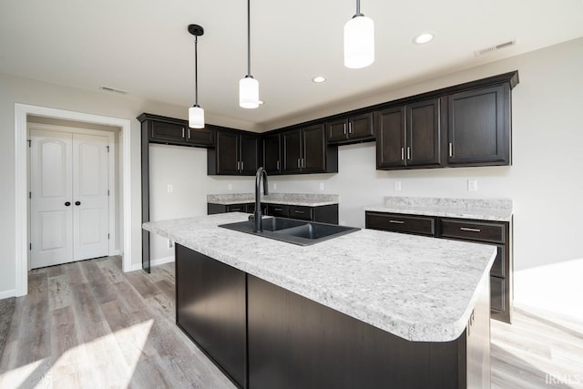 kitchen featuring pendant lighting, light hardwood / wood-style flooring, a kitchen island with sink, and sink