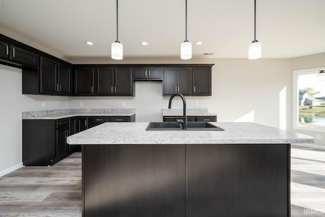 kitchen with decorative light fixtures, light hardwood / wood-style floors, a center island with sink, and sink