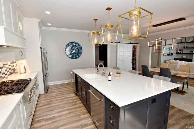 kitchen featuring a kitchen island with sink, sink, white cabinetry, hanging light fixtures, and stainless steel appliances