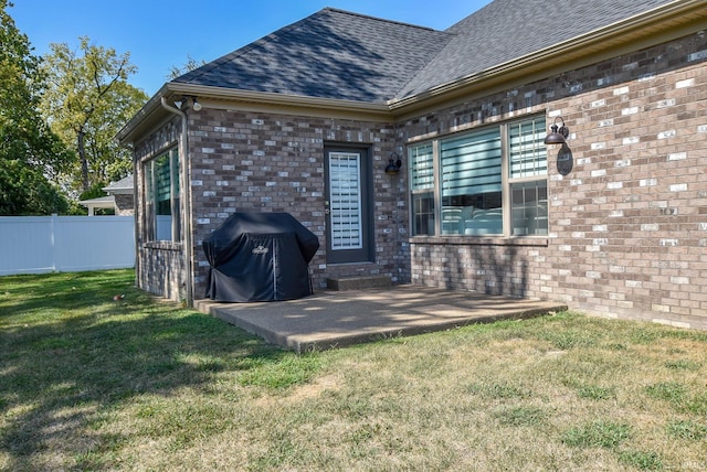 exterior space with a patio, fence, a yard, roof with shingles, and brick siding