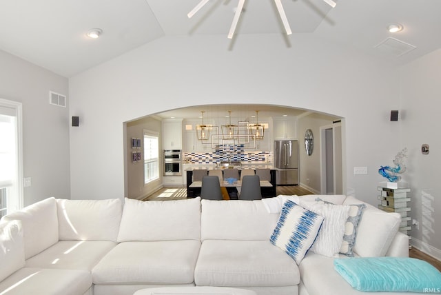 living area with vaulted ceiling, visible vents, arched walkways, and light wood finished floors