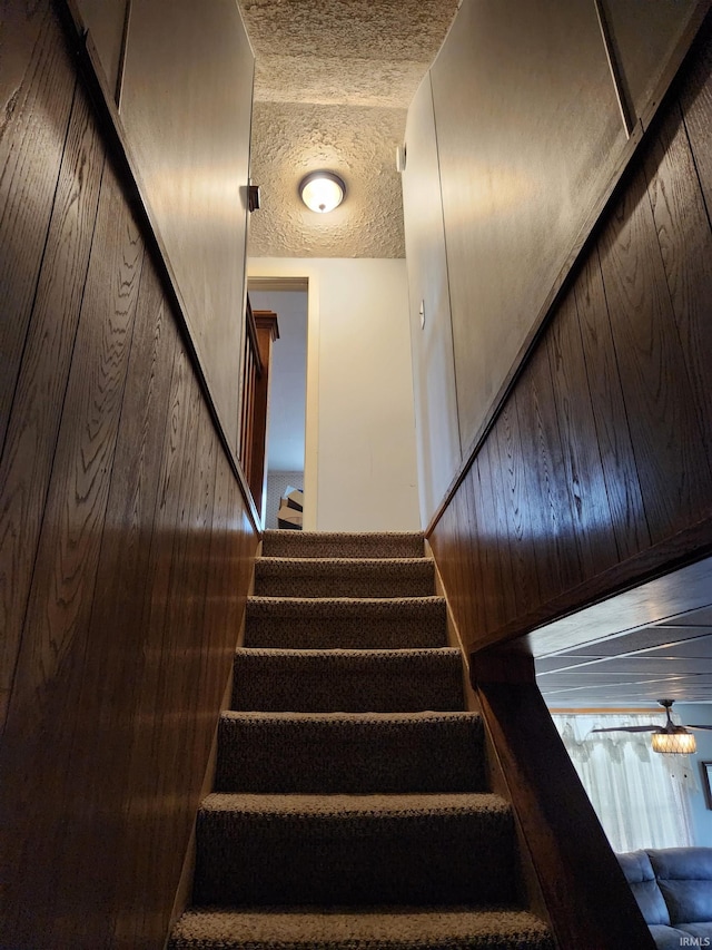 staircase featuring wooden walls, a textured ceiling, and hardwood / wood-style flooring