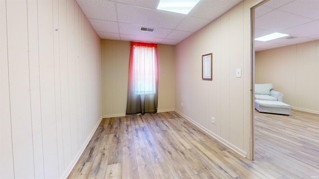 unfurnished room with wooden walls, light hardwood / wood-style flooring, and a drop ceiling