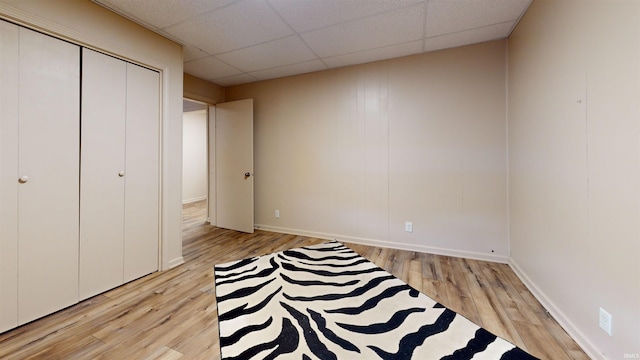 unfurnished bedroom with a drop ceiling, light wood-type flooring, and a closet