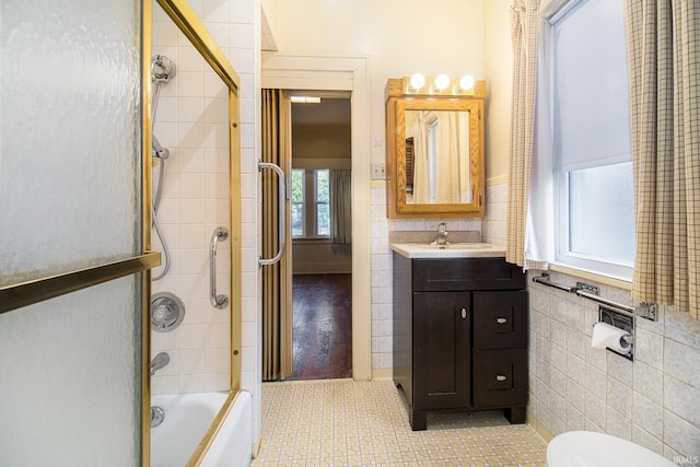 full bathroom featuring tile walls, vanity, shower / bath combination with glass door, hardwood / wood-style flooring, and toilet