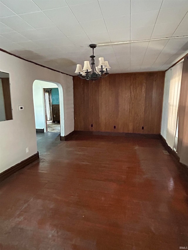 empty room featuring wood walls, an inviting chandelier, and dark wood-type flooring