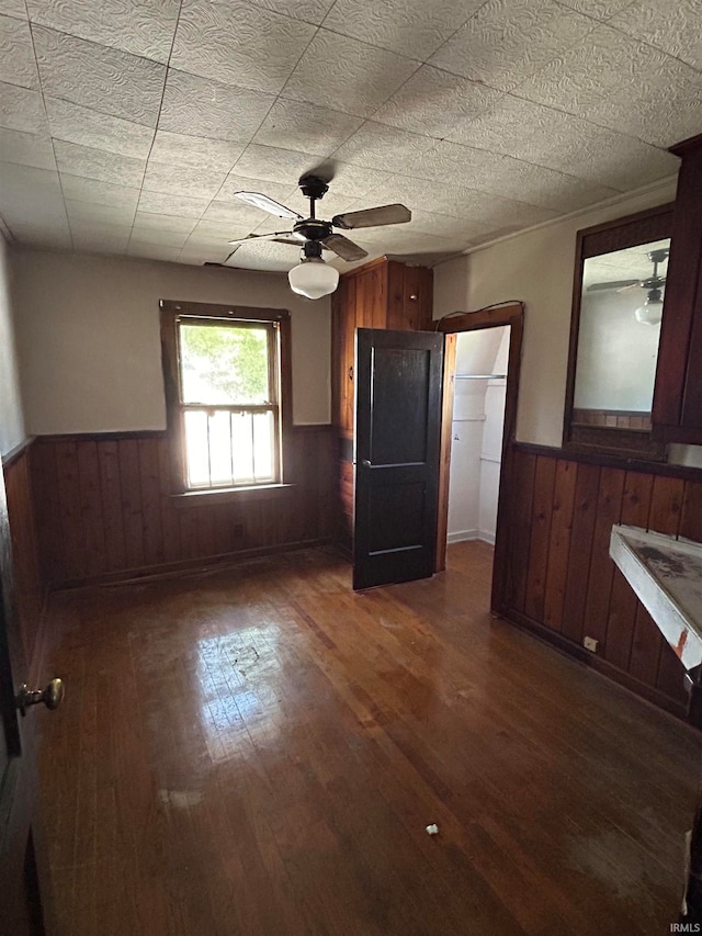 unfurnished bedroom featuring wooden walls, ceiling fan, dark wood-type flooring, and a closet