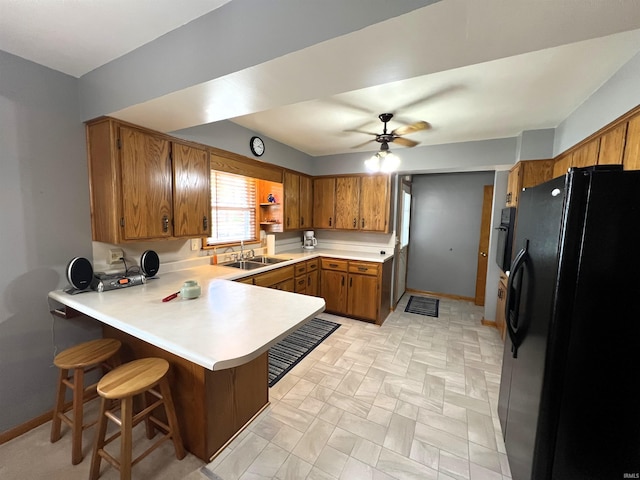 kitchen with kitchen peninsula, sink, black fridge with ice dispenser, ceiling fan, and a breakfast bar