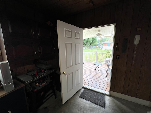 doorway with wood walls, ceiling fan, and concrete floors