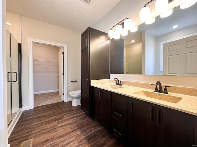 bathroom featuring a textured ceiling, a shower with door, hardwood / wood-style floors, vanity, and toilet