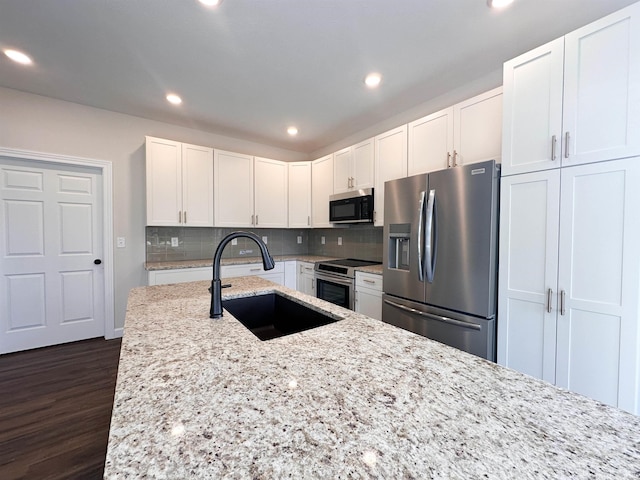 kitchen featuring tasteful backsplash, dark wood-type flooring, white cabinetry, stainless steel appliances, and light stone countertops