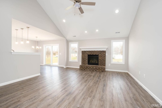 unfurnished living room featuring ceiling fan with notable chandelier, a wealth of natural light, a fireplace, and dark hardwood / wood-style flooring