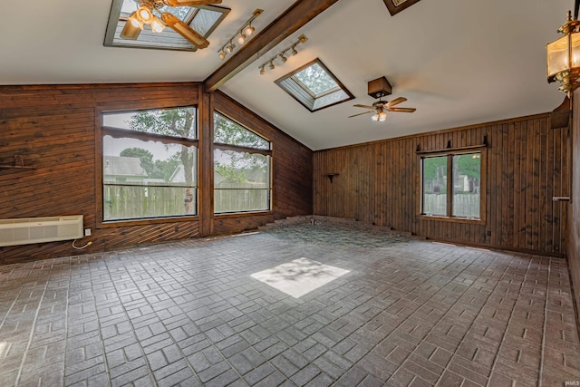 unfurnished living room featuring rail lighting, wooden walls, lofted ceiling with skylight, a wall mounted air conditioner, and ceiling fan