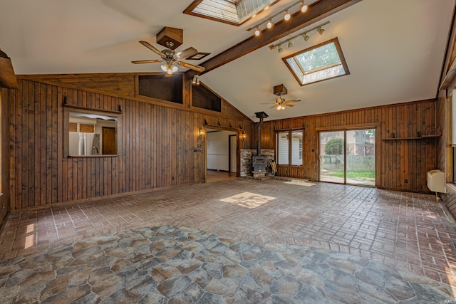 unfurnished living room featuring ceiling fan, wooden walls, and a wood stove