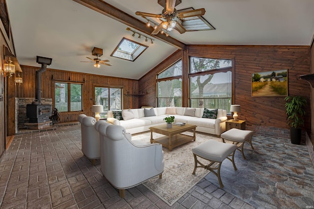 living room with a wood stove, wood walls, ceiling fan, and lofted ceiling with skylight