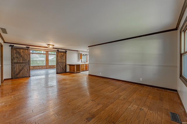 empty room with light wood-type flooring, crown molding, and a barn door