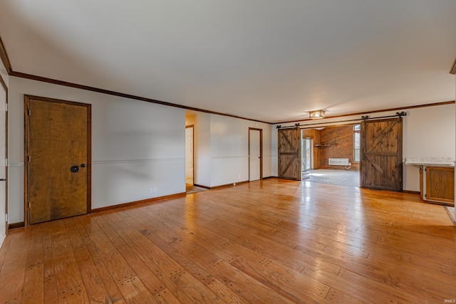 unfurnished living room with a barn door, light hardwood / wood-style floors, and ornamental molding