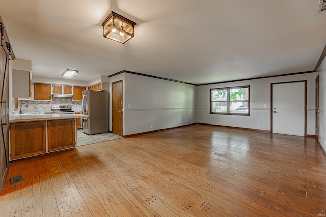 kitchen featuring light wood-type flooring, kitchen peninsula, decorative backsplash, appliances with stainless steel finishes, and ornamental molding