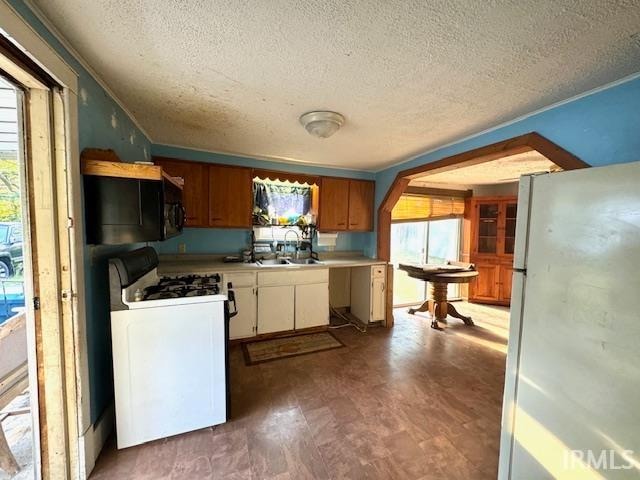 kitchen with a textured ceiling, wood-type flooring, white appliances, and a wealth of natural light