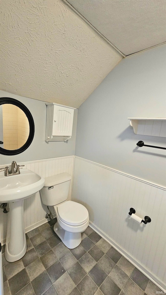 bathroom with vaulted ceiling, a textured ceiling, sink, and toilet