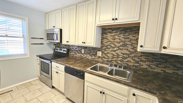 kitchen with dark stone counters, tasteful backsplash, sink, cream cabinetry, and appliances with stainless steel finishes