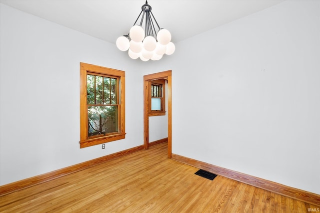 spare room featuring an inviting chandelier and light hardwood / wood-style floors