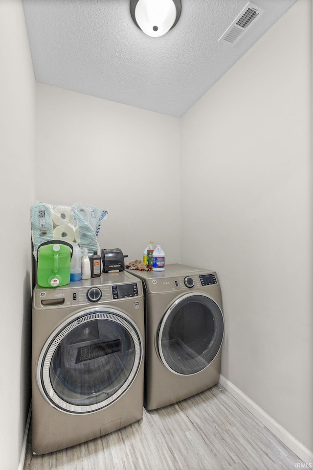 laundry area with light hardwood / wood-style flooring, a textured ceiling, and washer and dryer