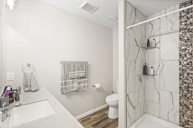 bathroom featuring a tile shower, a textured ceiling, hardwood / wood-style floors, and toilet