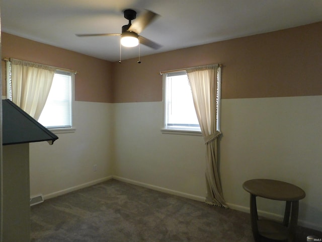 spare room with dark colored carpet, ceiling fan, and a healthy amount of sunlight