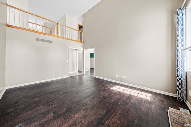 unfurnished living room featuring a towering ceiling and dark wood-type flooring