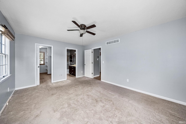 unfurnished bedroom with a closet, light carpet, a walk in closet, ensuite bathroom, and ceiling fan