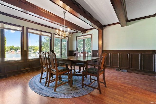 dining room featuring wood-type flooring, ornamental molding, a notable chandelier, and beam ceiling