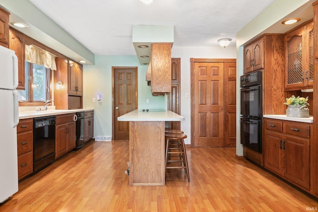 kitchen featuring black appliances, light hardwood / wood-style floors, a breakfast bar area, and sink