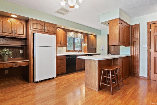 kitchen with light wood-type flooring, dishwasher, a breakfast bar area, kitchen peninsula, and white fridge