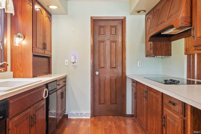 kitchen featuring black appliances, light hardwood / wood-style floors, custom range hood, and sink