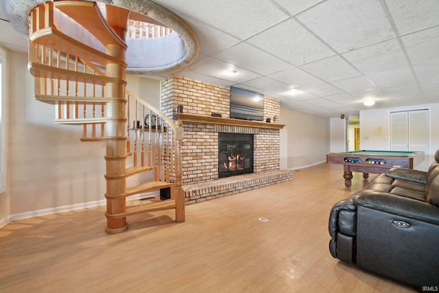 living room with pool table, hardwood / wood-style flooring, a drop ceiling, and a brick fireplace