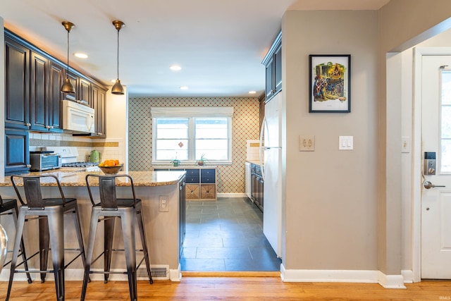 kitchen featuring hardwood / wood-style flooring, a kitchen bar, hanging light fixtures, white appliances, and light stone countertops