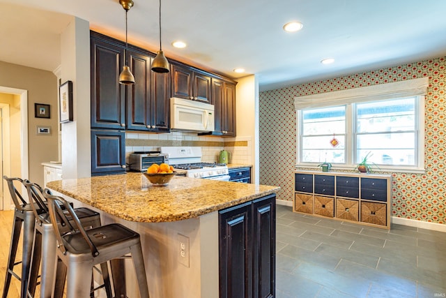 kitchen featuring hanging light fixtures, white appliances, a breakfast bar area, light stone countertops, and a center island