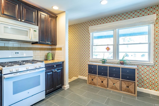 kitchen with dark brown cabinets, white appliances, backsplash, and dark tile patterned floors