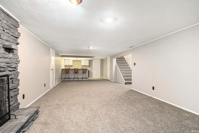 unfurnished living room with a textured ceiling, carpet, a fireplace, and crown molding