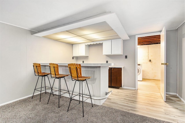 kitchen with washer / dryer, light hardwood / wood-style floors, white cabinets, kitchen peninsula, and a kitchen breakfast bar