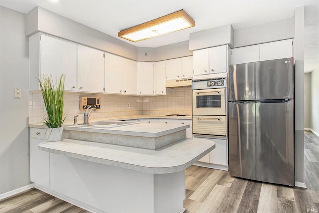 kitchen featuring white cabinetry, white appliances, kitchen peninsula, light hardwood / wood-style flooring, and sink