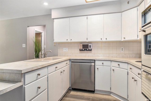 kitchen with decorative backsplash, white cabinets, light hardwood / wood-style flooring, stainless steel dishwasher, and sink