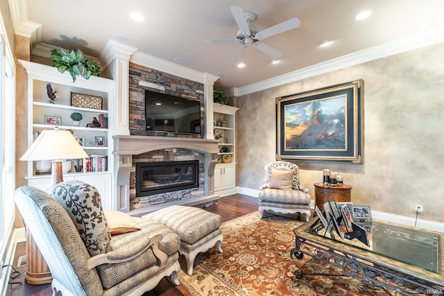 living room featuring dark wood-type flooring, a stone fireplace, crown molding, ceiling fan, and built in shelves