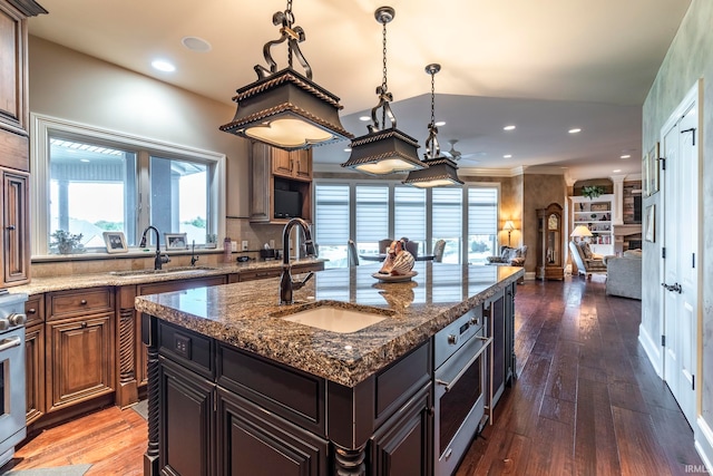 kitchen with dark wood-type flooring, sink, a kitchen island, dark brown cabinetry, and dark stone countertops