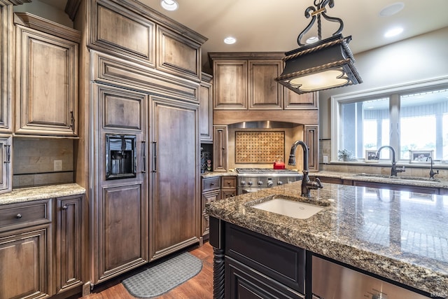 kitchen featuring wood finished floors, paneled built in refrigerator, backsplash, and a sink