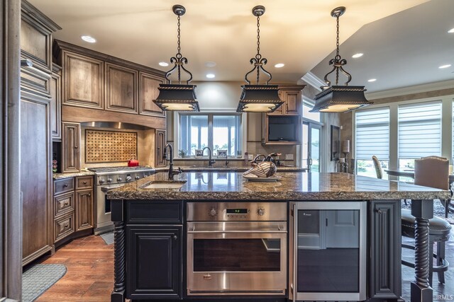 kitchen featuring sink, decorative light fixtures, a large island with sink, crown molding, and dark hardwood / wood-style flooring