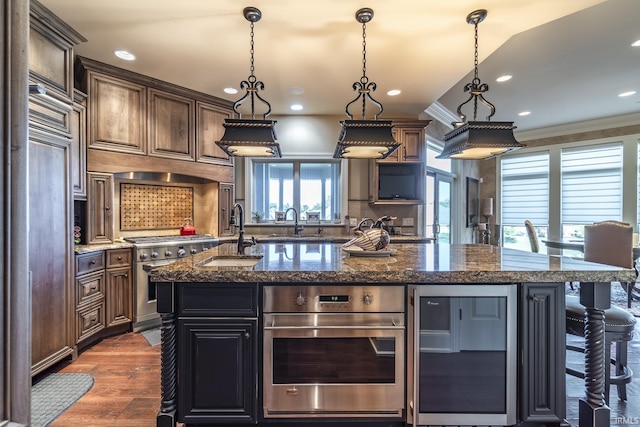 kitchen with dark wood finished floors, an island with sink, ornamental molding, stainless steel appliances, and a sink