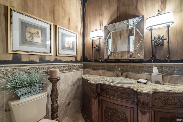 half bath with tile walls, wainscoting, toilet, and vanity