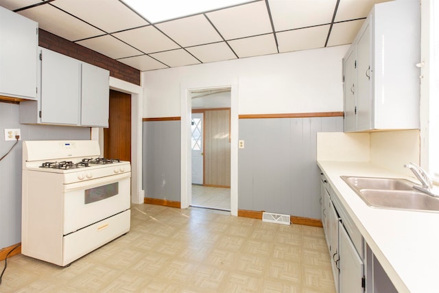 kitchen with wood walls, sink, white range with gas cooktop, and white cabinetry